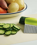 Crinkle cutter knife with green handle and stainless steel wavy blade on cutting board beside sliced cucumbers