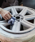 Close-up of a silver alloy car wheel rim being wiped with a blue cloth.