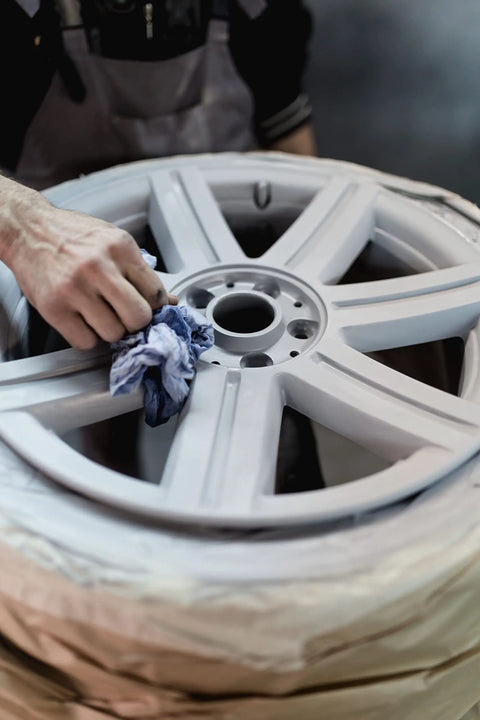 Person polishing a car alloy wheel, using a cloth for cleaning and detailing, focusing on the surface of the rim in a workshop setting.