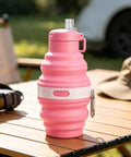 Pink foldable water bottle with leak proof locking lid for outdoor adventures on a wooden table.