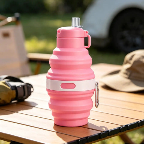 Pink foldable water bottle with leak proof locking lid for outdoor adventures on a wooden table.