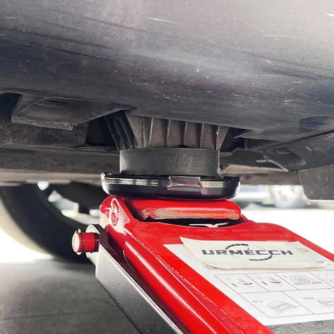 Close-up of rubber jack pad on a red floor jack lifting a vehicle, highlighting Dual Use Lifting Axle Saddle Adapter Pads, 2 Pack For BMW X3 X5 X6 X7 And Mini, No Fuss Fit, Compatible With 4 To 8 Ton Hydraulic Bottle Jacks And Floor Trolley Jacks, 1.42 Inch Recess, Rubber Jack Pad Pucks For Safer, Level Vehicle Lifting.