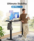 Man using Electric Standing Desk With Real Deal One Piece Desktop Adjustable Height For Sit Stand Four Memory Settings 48 By 24 Inches Heavy Duty Steel Frame Built To Last Home Office Desk Black in modern setting