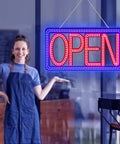 16.5 By 9 Inch Horizontal LED Open Sign For Biz hanging in a storefront with a smiling person in an apron nearby.