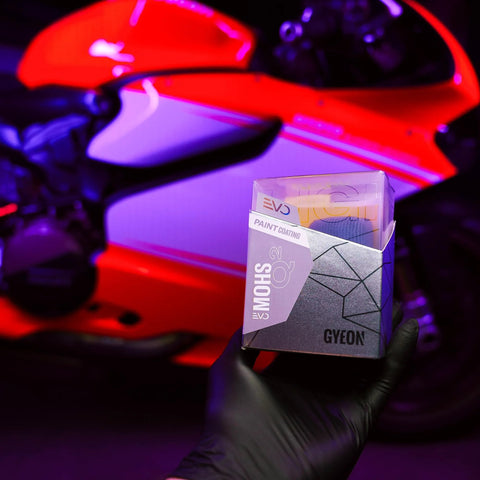 GYEON MOHS ceramic coating kit box held by gloved hand against a red motorcycle backdrop.