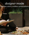 Person sitting with book on a wooden deck beside a large square plastic planter for indoor or outdoor use, durable all weather garden pot with drainage holes, dope decor for tall plants and trees, suits modern patios and decks.