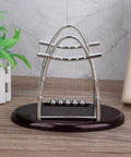 Pendulum Ball Desk Decor Set That Demonstrates Newton's Laws With Swinging Balls on wooden base with greenery in background