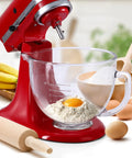Red stand mixer with glass bowl, flour, and egg, showcasing stainless steel mixing bowl for 4.5 to 5 quart KitchenAid tilt-head mixers.