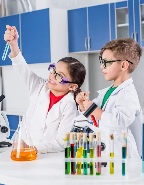 Two children in lab coats performing experiments in a science lab, wearing eyeglasses with side shields.