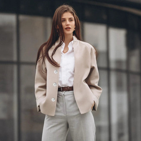 Fashionable woman in beige coat and white shirt standing in urban setting