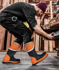 Person wearing Steel Toe Rubber Boots For Men With Puncture Proof Steel Shank Waterproof Insulated 6mm Neoprene Work Boots With Reflective Strips For Farming Manufacturing And Construction Black Orange Size 8, shown in a workshop setting.