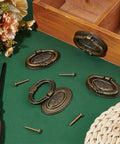 Four Pack Antique Oval Drawer Pulls In Antique Bronze, Vintage Floral Engraved Cabinet Handles displayed on green background with screws