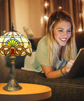 Tiffany Style Yellow Stained Glass Table Lamp with LED Bulbs, 12x12x19 inches, glowing warmly beside a woman reading on a tablet.