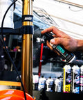 Applying Silky Suspension Serum 100ml Protective Spray for Bike Shocks and Seals, reduces stiction and friction, outdoor setting.