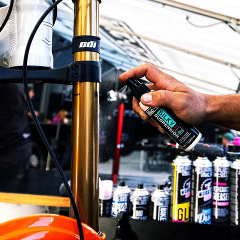 Applying Silky Suspension Serum 100ml Protective Spray for Bike Shocks and Seals, reduces stiction and friction, outdoor setting.