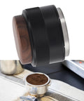 Top Tier 51Mm Black Coffee Distributor And Espresso Tamper For Baristas Stainless Steel Tool on a table next to coffee grounds.