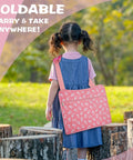 Child outdoors carrying the Kids Travel Tray for Car Seat with Ipad Holder and Dry Erase Board, pink with floral pattern.