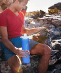 Man holding Ultra Lightweight Foldable Water Bottle For Hiking And Outdoor Adventures, sitting on rocks