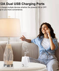 Woman using phone next to Coastal Glass Table Lamp with Rattan Wicker, Built-In USB Ports on a living room table.