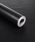 Thick Black Peel And Stick Wallpaper Roll Featuring Hella Durable Self Adhesive PVC Material For Quick Interior Wall Covering With Zero Residue Guarantee on a black surface.