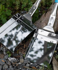 Heavy Duty Wood Stove Ash Shovel With 14.6 Inch Rust Resistant Blade, Blue Handle, Stainless Steel Scoop And Hanging Hook For Fire Pit BBQ Campfire Cleanup, Easy Pile And Sift Ashes Safely, resting on pebbles beside a tree.