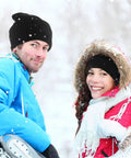 Couple smiling in snow, wearing black knit hats and winter jackets, showcasing Three Hole Knit Ski Mask Balaclava for Winter Warmth