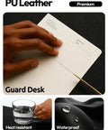 Hand writing on a notebook placed on a Leather Office Desk Pad Protector, Large Non Slip PU Leather Mouse Pad And Writing Desk Blotter, Waterproof Guard For Home And Office, Scratch Spill And Heat Resistant, 23.6 By 13.8 Inches, Black