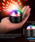 Person holding Mini Disco Ball Light Rechargeable Party LED Lamp With Sound Activated Strobe DJ Mode, projecting colorful lights.