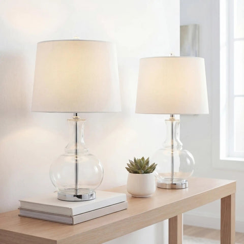 25 Inch Clear Chrome And Brass Glass Table Lamps Set Of 2 With White Linen Drum Shades on a Wooden Table