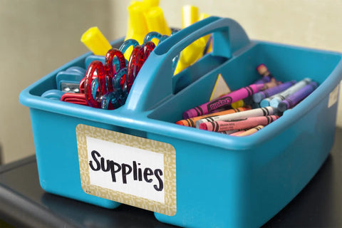 Classroom supplies in a blue plastic caddy labeled with Classroom Cottage Name Tags And Labels Multi Pack For Teachers.