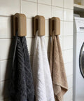 Premium Wall Mount Automatic Locking Towel Hook With Smart Space Saving Design And No Sweat Storage For Daily Grind In Slick Matte Black Finish For Any Modern Setup, holding three towels.