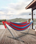Man relaxing in Easy Setup Brazilian Style Hammock With Tree Straps For Hanging, Blue And Red Stripe, on patio by lake.