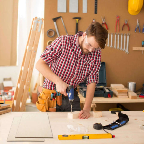 Basswood sheets for crafts on workbench; man in plaid shirt drills a wooden block.