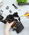 Robotic arm kit with Arduino-style 5-DOF control board, black joints, wires, and screwdriver assembling on grid mat.