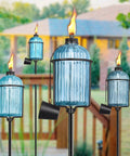 4 Pack Glass Garden Torch Set with 13.5 Oz Citronella Oil, 61 Inch Adjustable Blue Outdoor Torches installed along patio pathway