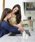 Mother and daughter using a kitchen sink with 17 Pack Travel Toiletry Pouches Leak Proof TSA Approved Stand Up Refillable Travel Containers on counter.