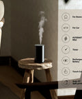 Waterless Essential Oil Diffuser Starter Kit With Four 10mL Hotel Scent Fragrance Oils Battery Operated Portable Diffuser For Home Car Office AN8 Kit Black on wooden stool, emitting mist.