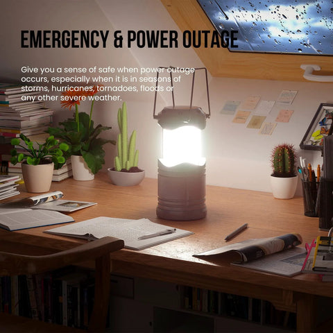 Front view of Lichamp LED camping lantern, gray, battery-powered, on a wooden desk beside plants