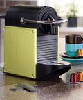 Compact yellow and black espresso machine with coffee cups and pods on a kitchen counter, showing modern design.