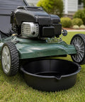 Huge 7 Qt Oil Drain Pan With Built Scale, Leak Proof Spout And Splash Guard Lets You Grab Used Motor Oil Quick Without Mess Or Hassle For Your Garage Game positioned under a lawn mower on grass.