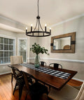 Six Light Wagon Wheel Chandelier In Black Industrial Farmhouse Style hanging over dining table in bright room