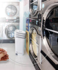 Hand holding Stainless Steel Washing Machine Door Boot Spring Clamp For Front Load Washers near a washer in a laundromat.