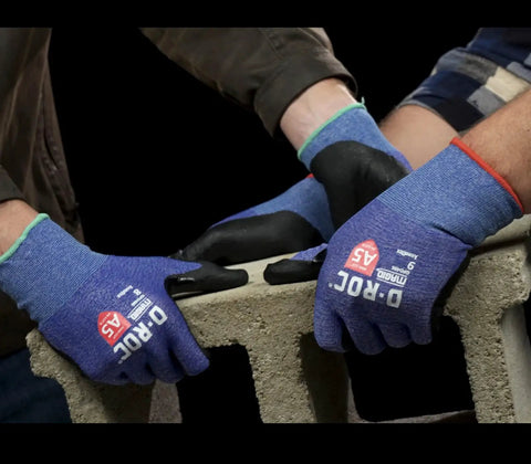Workers wearing AeroDex 18 Gauge ANSI A5 Cut Resistant Work Gloves with Foam Nitrile Palm Coating, handling concrete block.