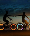 Two cyclists with illuminated wheels at sunset showcasing 72Pcs Spoke Reflectors Set for Night Riding Red Reflective Spoke Skins