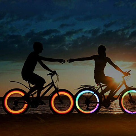Two cyclists with illuminated wheels at sunset showcasing 72Pcs Spoke Reflectors Set for Night Riding Red Reflective Spoke Skins