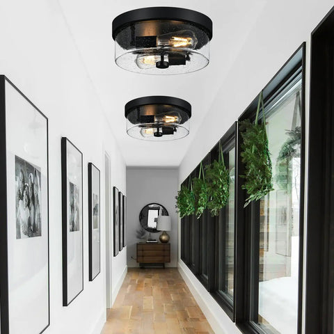 Two Light Black Flush Mount Ceiling Light Fixture With Seeded Glass Shade installed in hallway with decor and artwork