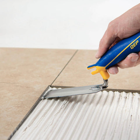 Person using Comfort Grip 6 In By 2 In Flat Margin Flooring Trowel With Bucket Hook on thinset between tiles.