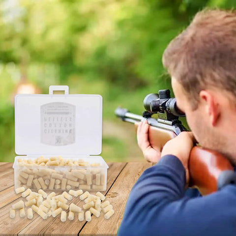 A shooter aims with a rifle beside a box of 300 Count.25 Caliber Airgun Cleaning Pellets In Cotton Wool Felt, on a wooden table.