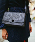 Woman carrying a black embossed leather shoulder bag on the street, wearing a navy coat.