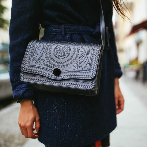 Woman carrying a black embossed leather shoulder bag on the street, wearing a navy coat.